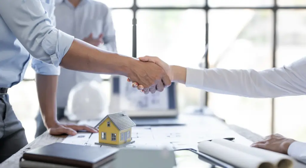 Handschlag über Hausmodell und Bauplänen – Lick & Partner Immobilien steht für Vertrauen und persönliche Immobilienberatung
